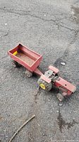 Photo of a red vintage metal Tonka tractor with a red trailer attached, showing wear and dirt, on pavement.