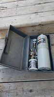 Top view of metal storage case open showing propane cylinder, torch heads, and coiled hose.