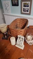 Photo showing the wooden picnic basket, pillar candle, decorative candle holder with scroll design, and a lamp or candle holder with beige shade.