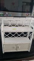 White wicker shelf with two open shelves and two bottom drawers, viewed frontally with a dark background.