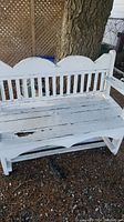 Front angled view of white wooden bench showing backrest design, armrests, seat wear and paint chipping.
