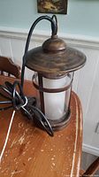 Side view of the 12 inch yard light lantern showing the bronze finish and glass cylinder within metal frame, with attached black electrical cord.