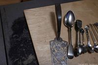 Full view of all 10 sterling silver serving pieces, including cake lifter, tongs, large spoon and 8 smaller spoons.