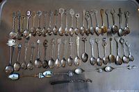 Full collection of 46 souvenir spoons laid out on a flat surface, showing variety in size and design.