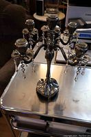 Front angle of silver-toned 5 candle 4 arm candelabra with hanging crystal accents on each arm, placed on a metal table.