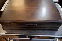 Closed wooden cutlery box with dark finish and metal handle, showing wear