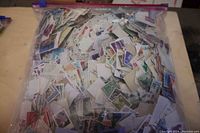 Large resealable plastic bag filled with assorted small postage stamps from worldwide origins, showing a variety of colors and designs.