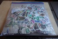 Full view of a large clear ziplock bag filled with hundreds of assorted postage stamps from various countries. The stamps vary widely in color and design.