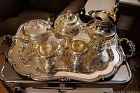 Full view of large silver plated Victorian tea set on ornate engraved tray showing coffee pot, tea pot, cream pitcher, sugar bowl, and water pitcher.