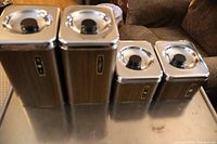Set of four metal kitchen canisters with wood-grain finish and silver lids, displayed on a table.