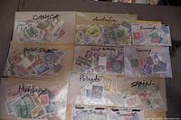 Photo showing multiple glassine envelopes each labeled with a country name containing assorted used stamps: Canada, Australia, Finland, United States, Great Britain, Germany, Hungary, Poland, Spain, Cook Islands, Denmark.