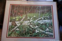 Full view of framed signed print showing trilliums with fallen birch logs and forest floor in background.