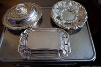 Overview photo showing the collection of silver-plated pieces including the lidded serving dishes, footed bowl, and rectangular trays.