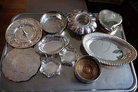 Top view of all 10 silver plated pieces arranged on metal surface, showcasing variety of shapes and patterns including trays, bowls, candy dishes, and decorative heart box.