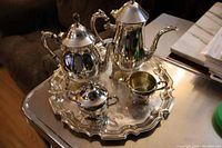 Silver plated tea set on tray showing tea pot, coffee pot, creamer, sugar bowl with lid, and tray with scalloped edge.