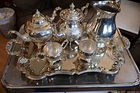 Full view of silver plate tea set on large rectangular engraved tray, showing teapot, coffee pot, creamer, sugar bowl and water pitcher.