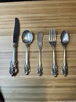 Five silver flatware pieces arranged on a wood surface