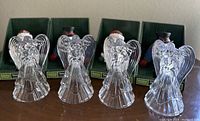 Four clear glass angel stocking holders displayed side by side against backing boxes with Santa and Snowman images.