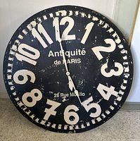 Front close-up of the large round wooden wall clock face showing black background, large white distressed numerals, and French text.
