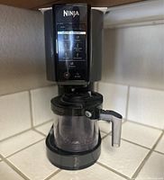 Front angle showing black Ninja NC301 CREAMi ice cream maker with clear mixing container and handle on kitchen counter.