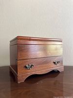 Closed view of the wooden jewelry chest showing polished wood finish, lower drawer, and feet design.