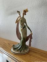 Side view of the porcelain statue showing the woman holding a theatrical mask and elevated on a wooden base, with dress flowing and decorated.