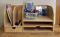 Front view of vintage wooden desk organizer with divider compartments holding office supplies including colorful scissors in plastic container, markers, and notepad.