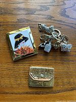 Image showing the full lot of three items on a wooden surface: decorative makeup mirror, sequin coin purse, and silver-tone charm keychain