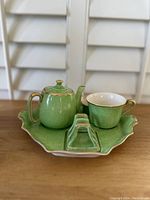 Front view of the tea set showing teapot, teacup, and scalloped tray with green crackled glaze and gold accents.