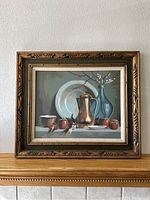 Front view of framed paint-by-number still life painting featuring copper pitcher, white plate, blue vase with blossoms, apples on table