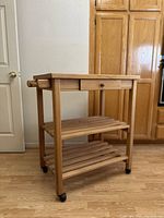 Wooden butcher cart angled view showing the drawer, towel rack, and slatted shelves on caster wheels.