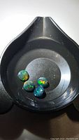 Four calibrated black opal gemstones shown in a black container, displaying vivid rainbow play of color with dark grey/black body tone