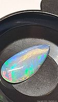 Pear-shaped Ethiopian opal cabochon with vivid play of color in black container.