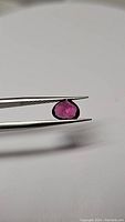 Photo of 1.74ct teardrop cut Malawi garnet held in tweezers showing deep pink purple color and clarity.