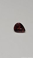 Close-up photo of pear-shaped reddish-brown faceted gemstone (African zircon) on a neutral background.