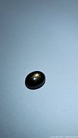 Photo showing oval black star sapphire cabochon with star flash effect on blue background.