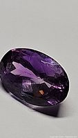 Close-up image of an oval cut Brazilian amethyst gemstone showing facets and deep violet color.