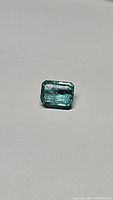 Clear photo of rectangular emerald cut natural Columbian emerald gemstone with visible inclusions.