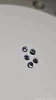 Five round diamond cut tanzanite gemstones on a reflective surface, showing color and size range 3.5-4mm