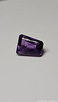 Photo of deep purple tapered baguette cut amethyst gemstone placed on a flat surface.