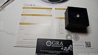 Moissanite ring in black box alongside official GRA grading report showing 1ct, VVS1, D color grading details and signature.