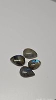 Four pear-shaped labradorite cabochons with blue flash effect on a plain white surface.
