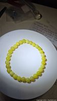 Natural lemon jade bead bracelet placed on a white circular surface, showing the uniform round beads and their color.