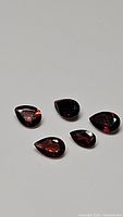 Five natural cherry red Mozambique garnet pear cut gemstones lying on a flat surface with visible facets.