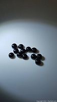 Twelve black round cabochon beads displayed against a plain white surface under bright lighting, showing polished smooth round surfaces and uniform size.