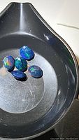 Five oval faceted natural black opal gemstones with vivid rainbow flashes placed in a black tray, showing vibrant colors and clarity of stones.