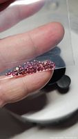 Multiple small round cabochon cut Rhodolite garnet gemstones held on fingers under magnification, showing color and slight inclusions.