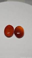 Top view of two polished oval carnelian stones with deep orange-red color on white background.