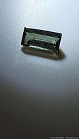 Close-up photo of natural green tourmaline baguette cut gemstone showing its color, shape, and clarity on a white textured background.