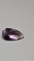 Pink amethyst pear shape checkerboard cut gemstone 20x10mm on gray background, showing facets and natural color.